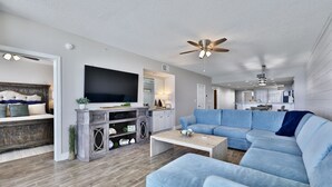 A spacious living room with a large sectional sofa, a flat-screen TV, and a ceiling fan.