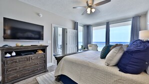 A bedroom with a large bed, a flat-screen TV, a wooden dresser, and a view of the ocean.