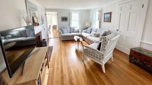 A living room with a TV, sofa, and armchair, wooden flooring, and a door. - Cozy Chatham home with privacy and nautical decor (Chatham)
