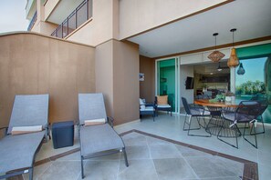 A patio area with two lounge chairs, a dining table with chairs, and a kitchen visible through an open door.