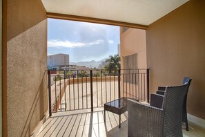 A balcony with a view of a cityscape, a table, and two wicker chairs. - 1BR with 2 Balconies + Views @ Grand Venetian (Puerto Vallarta)