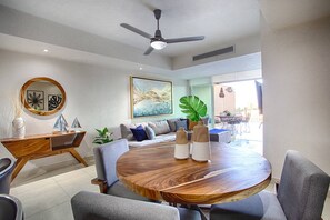 A modern living room with a round wooden dining table, grey sofas, and a ceiling fan. - 1BR with 2 Balconies + Views @ Grand Venetian (Puerto Vallarta)