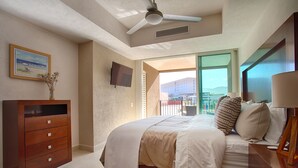 Un dormitorio con cama, cómoda, televisor y vistas al exterior.