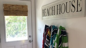 Una porta con un cartello che riporta la scritta 'BEACH HOUSE', una finestra con persiana in bambù e un porta-asciugamani con asciugamani a righe.