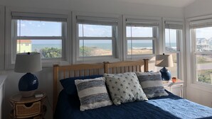 Una camera da letto con un letto, due comodini, una ventola a soffitto e ampie finestre con vista sulla spiaggia.