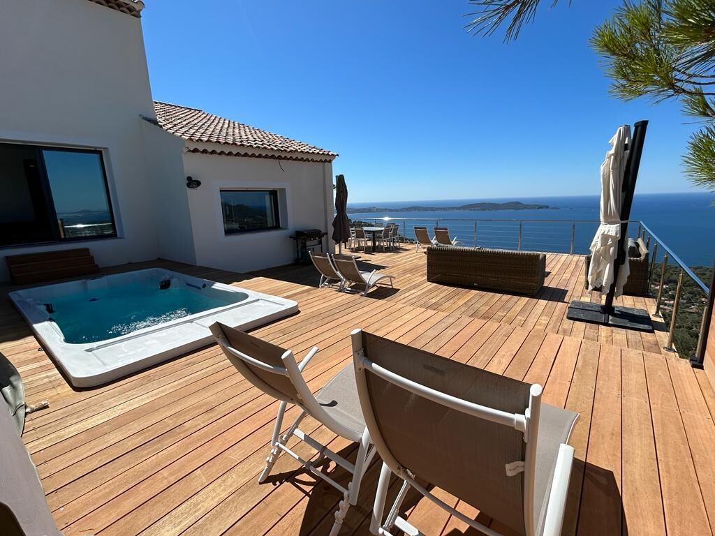 A wooden deck with a hot tub, lounge chairs, and a view of the sea.