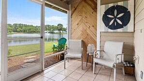 A room with a sliding glass door leading to a view of a lake and green chairs outside.