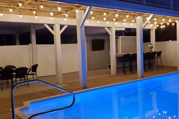 The outdoor oasis - heated pool, tiki bar, dining area, and TV.