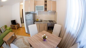 Un espace de vie compact comprenant une kitchenette, un coin repas et un canapé vert.