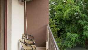 Un balcon avec une chaise, un appareil de climatisation et une vue sur un immeuble et des arbres.