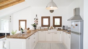 Cozinha moderna com armários brancos, bancadas de madeira, geladeira de aço inoxidável e luminária pendente.