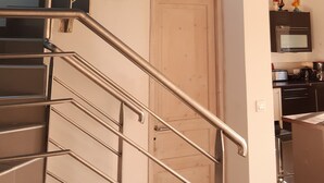 Ein modernes Interieur mit einer Treppe, die zu einer oberen Ebene führt, einer Holztür und einem Küchenbereich mit Geräten.