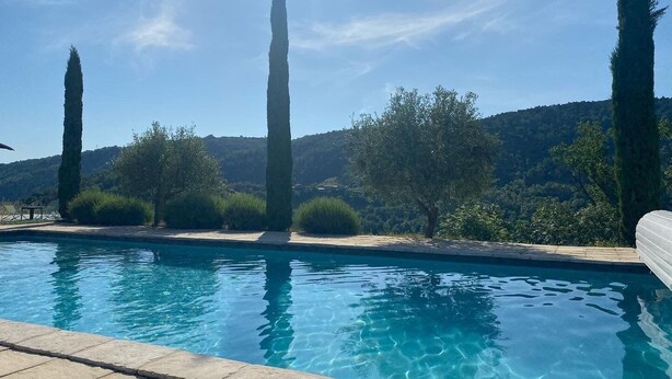 En swimmingpool med klart, blåt vand, omgivet af grønt og bakker i baggrunden.