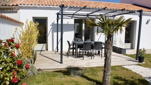 Un patio con una mesa, sillas, una pérgola y una palmera.