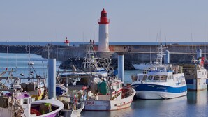Un puerto con barcos amarrados, un faro y un rompeolas rocoso.