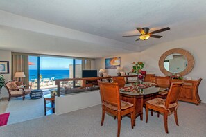 A spacious living area with a balcony overlooking the ocean, a dining area with wooden furniture, and a ceiling fan.