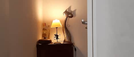 Un pasillo con una lámpara sobre una mesita de madera, un aplique de pared y una puerta.