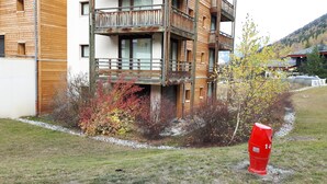 Un immeuble en bois à plusieurs étages, doté de balcons, entouré d’un feuillage automnal et agrémenté d’une borne d’incendie rouge.