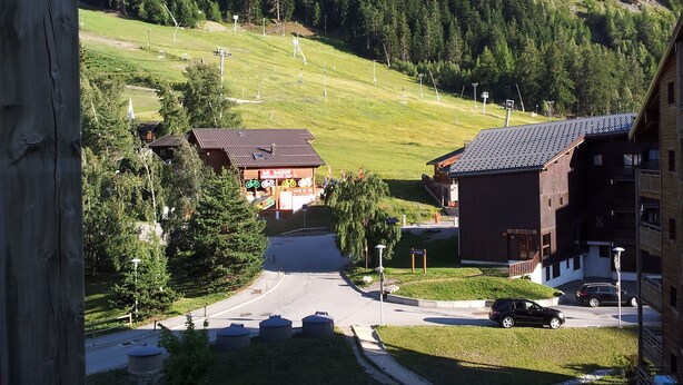 Une vue depuis un balcon donnant sur un paysage verdoyant, avec une piste de ski, des bâtiments et une route.