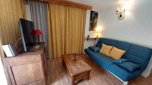 Un salon chaleureux avec un canapé bleu, une table basse en bois et un téléviseur posé sur un meuble en bois.