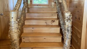 Una escalera de madera de diseño rústico, flanqueada por troncos de árboles cubiertos de arpillera, que conduce a una puerta con vistas al verdor exterior.