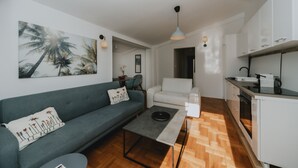 En moderne stue med en grå sofa, et sofabord og et køkken med hvide skabe og trægulv.