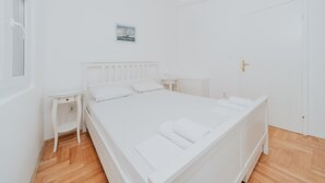 Et hvidt soveværelse med seng, sengebord, natbord, radiator og en dør.