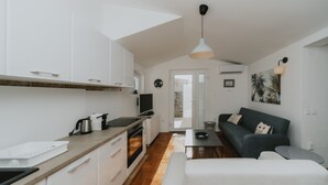 Et moderne køkken med hvide skabe, en træbordplade og en indbygget ovn. Der er et spiseområde med en mørkegrøn sofa og et lille bord.