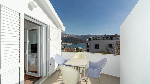 En balkon med et bord og stole, en skydedør samt udsigt over en sø og bjerge.