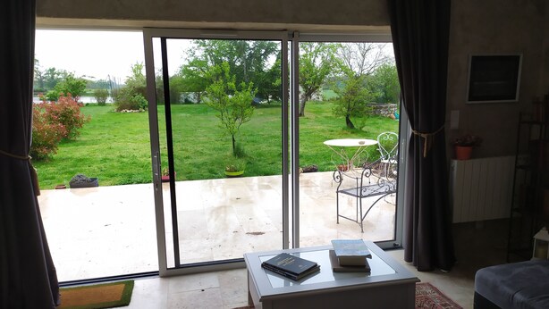 Een woonkamer met een schuifdeur die uitkomt op een terras. Er staat een witte salontafel met boeken, een tapijt met een patroon en een donkere bank.