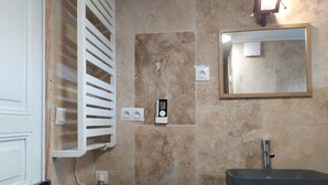 Een badkamer met een beigekleurige betegelde muur, een witte handdoekhouder, een wastafel en een spiegel.