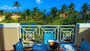 Een balkon met een eettafel, met uitzicht op een golfbaan en palmbomen.