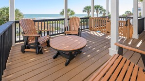 A wooden deck with two Adirondack chairs and a round table, overlooking a beach with palm trees and the ocean. - Oceanfront 5 BR Beach House in Surfside Beach with Private Pool! LA ESMERALDA II (Surfside Beach)