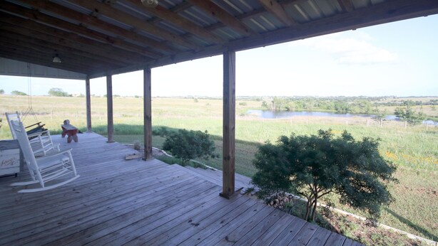 A wooden deck with a view of a lake and fields. - Beer Joint at the Brown Ranch (La Grange)