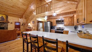 A spacious kitchen with wooden cabinets, a large island with bar stools, and modern appliances. - Holiday Road! Cabin with Beautiful Outdoors, Game Room and Hot Tub (Broken Bow)