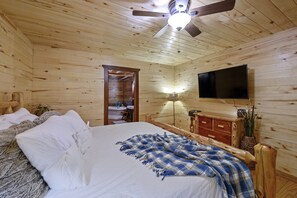 Un dormitorio de cabaña de madera con cama, televisor, ventilador de techo y cómoda de madera.