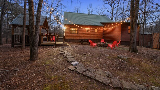 A log cabin with a stone pathway leading to a porch with red chairs. - Holiday Road! Cabin with Beautiful Outdoors, Game Room and Hot Tub (Broken Bow)
