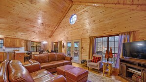 A cozy wooden interior with a leather sofa, a television, and a dining area. - Holiday Road! Cabin with Beautiful Outdoors, Game Room and Hot Tub (Broken Bow)