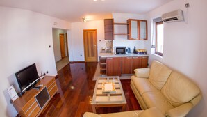 A compact living space with a sofa, a coffee table, a TV, and a kitchenette. - Lux Panoramic Apartment (Budva)