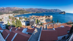 A coastal town with terracotta-roofed buildings, a marina, and mountains in the background. - Lux Panoramic Apartment (Budva)