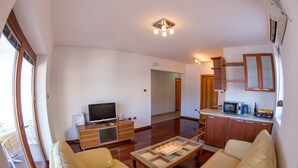 A living room with a sofa, a coffee table, a TV, and a kitchen area with cabinets and a microwave. - Lux Panoramic Apartment (Budva)