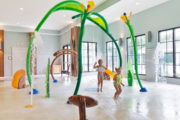 A water play area with green and yellow play structures, a sign reading "Kingston Plantation," and a large window in the background. - 2507 Margate - 4 bedroom ocean front condo - (Myrtle Beach)