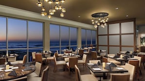 A restaurant with tables and chairs arranged for dining, large windows offering a view of the ocean, and hanging light fixtures. - 2507 Margate - 4 bedroom ocean front condo - (Myrtle Beach)