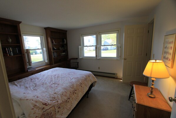 A bedroom with a large bed, two windows, a wooden dresser, and a lamp.