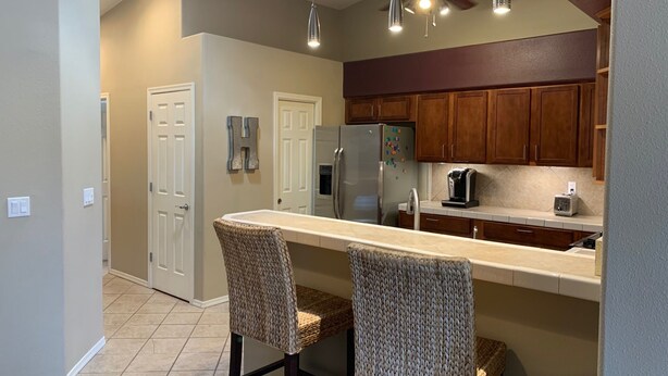 A kitchen with a central island, two bar stools, wooden cabinets, a refrigerator, and a ceiling fan. - Bullhead City 3 Bedroom! Private Launch, & Beach! (Bullhead City)