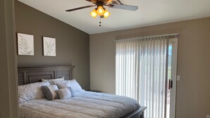 A bedroom with a large bed, a ceiling fan, and a view of the outdoors through a sliding glass door. - Bullhead City 3 Bedroom! Private Launch, & Beach! (Bullhead City)