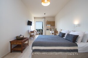 Ein Schlafzimmer mit Bett, Schreibtisch, Stuhl, Fernseher und einer Küchenzeile.