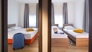 Een hotelkamer met twee bedden, een koffer en een laptop op een van de bedden.