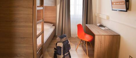 A dormitory room with a bunk bed, a desk, and a chair. There is a backpack and a pair of sneakers on the floor.