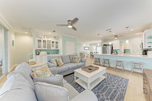 A spacious living room with a grey sofa, a coffee table, and a patterned rug.